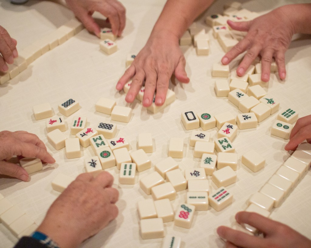 Hands shuffling American Mahjong tiles during game setup.