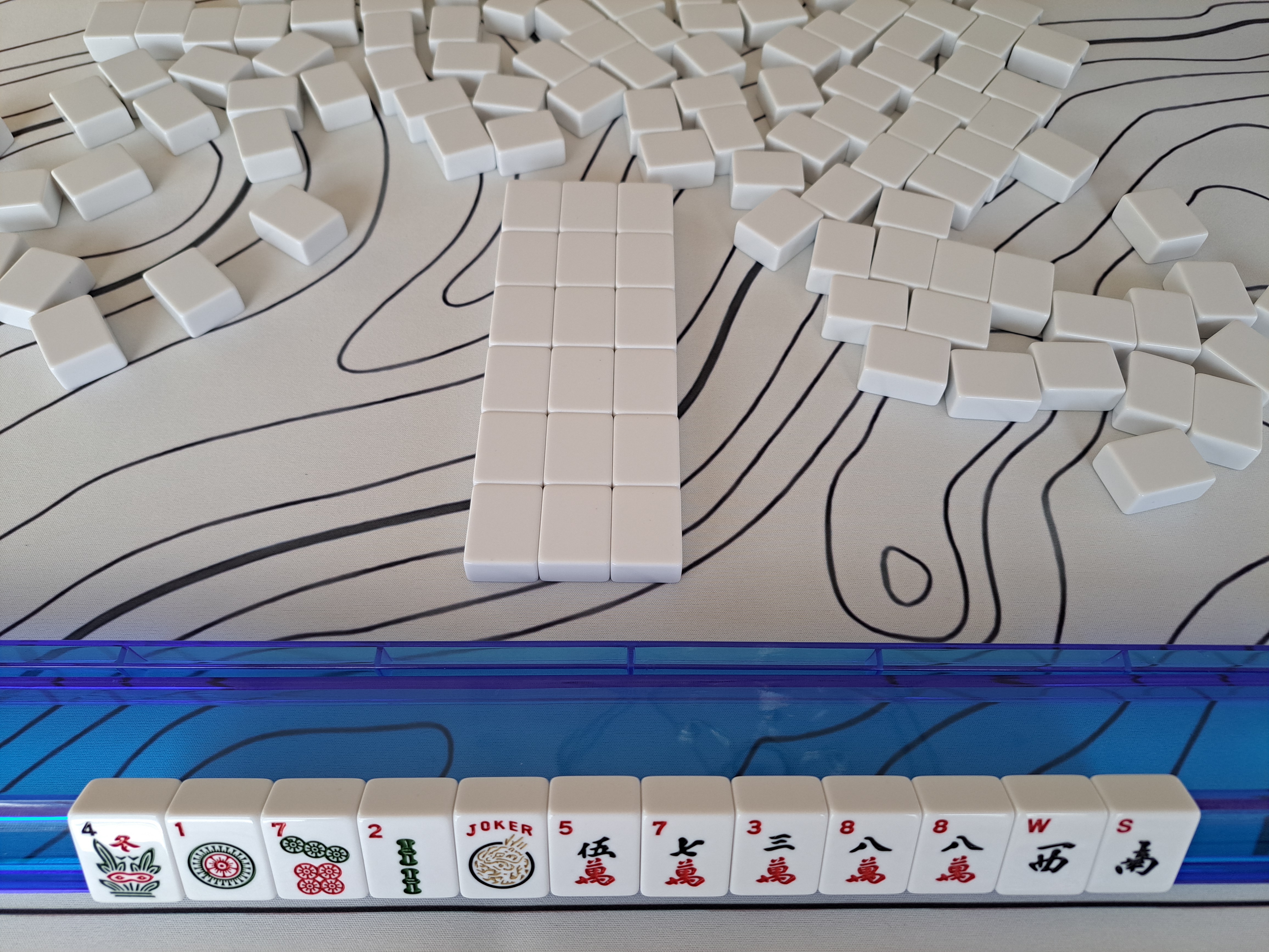American Mahjong setup showing 13 tiles arranged on a blue rack with six rows of tiles laid out on the mat for practicing solo Charleston strategy.